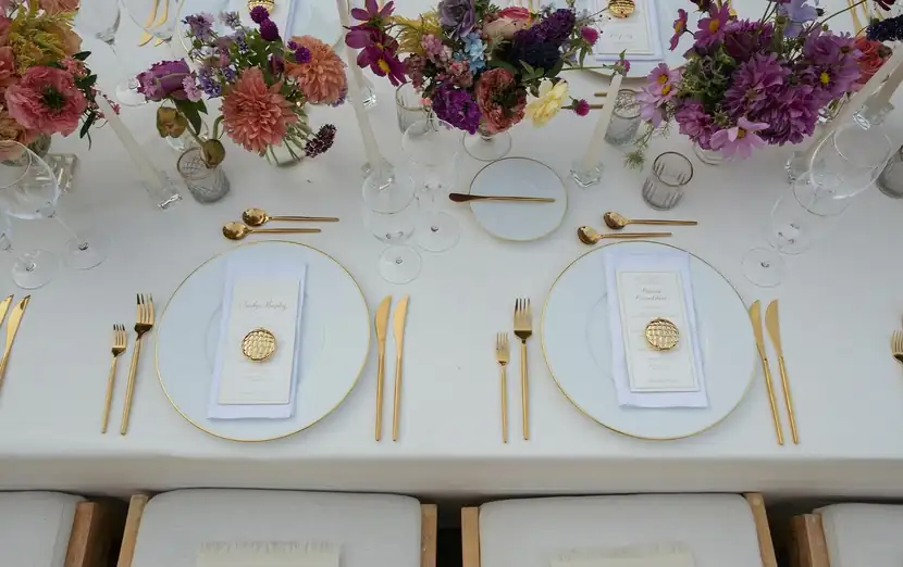 Long white table set with gold flatware, ivory linens and jewel-toned florals