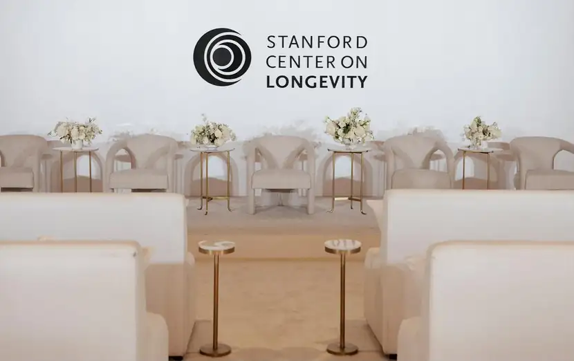 Cream-and-gold stage set with lounge seating beneath the Stanford Center on Longevity mark