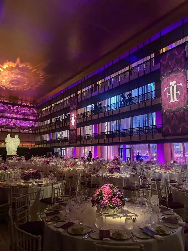 Ballroom set with round tables and floral centerpieces beneath saturated projection lighting
