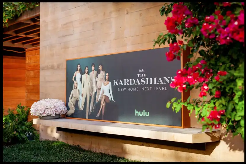 The Kardashians billboard installed in a landscaped courtyard beside bougainvillea