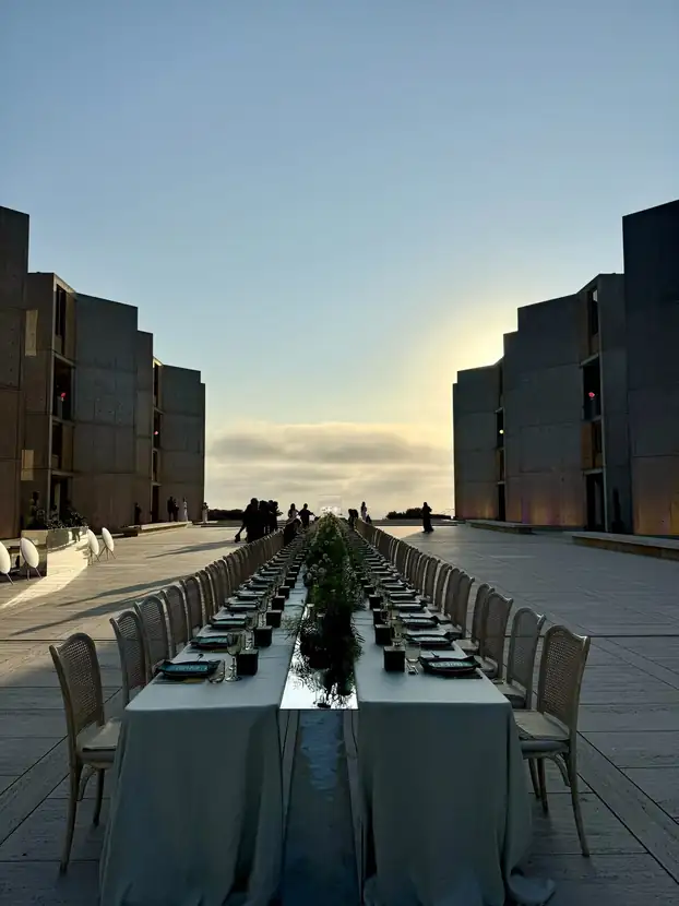 Two long banquet tables flanking the Salk Institute water channel at sunset