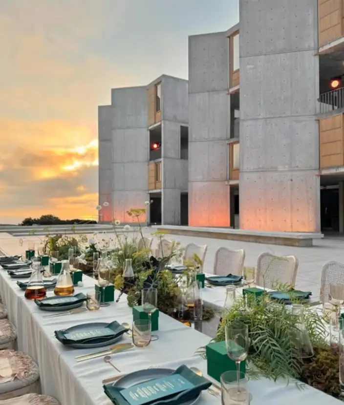 Dinner table dressed in white linen and greenery with the ocean sunset beyond
