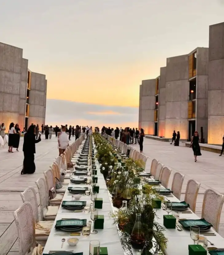 Guests seated at a long table in the courtyard as the sun sets over the Pacific