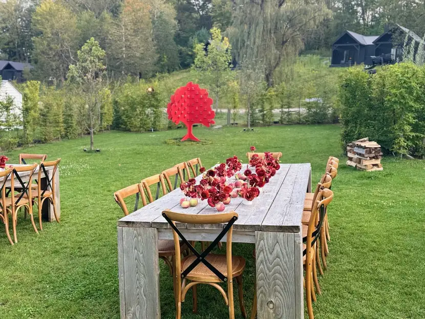 A long scarlet dinner table and red sculptural tree standing in an open green field