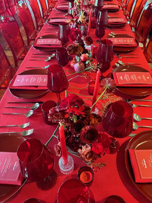 A long red banquet table set with red glassware, menus and floral runners