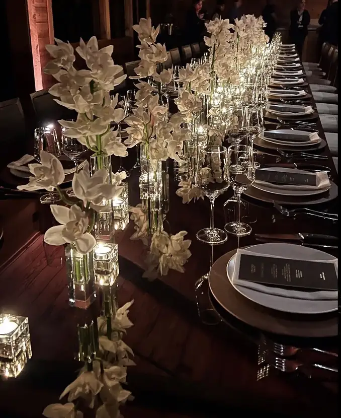 Overhead view of a dark wood table dressed with white orchids, crystal and candlelight