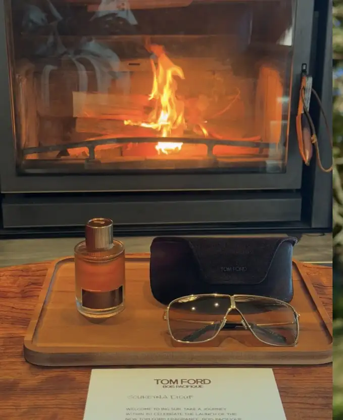 Fragrance bottle and eyewear staged on a wooden tray beside a lit fireplace