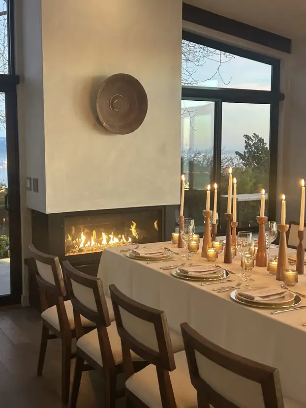 Long candlelit dinner table set before floor-to-ceiling windows at sunset over the ocean