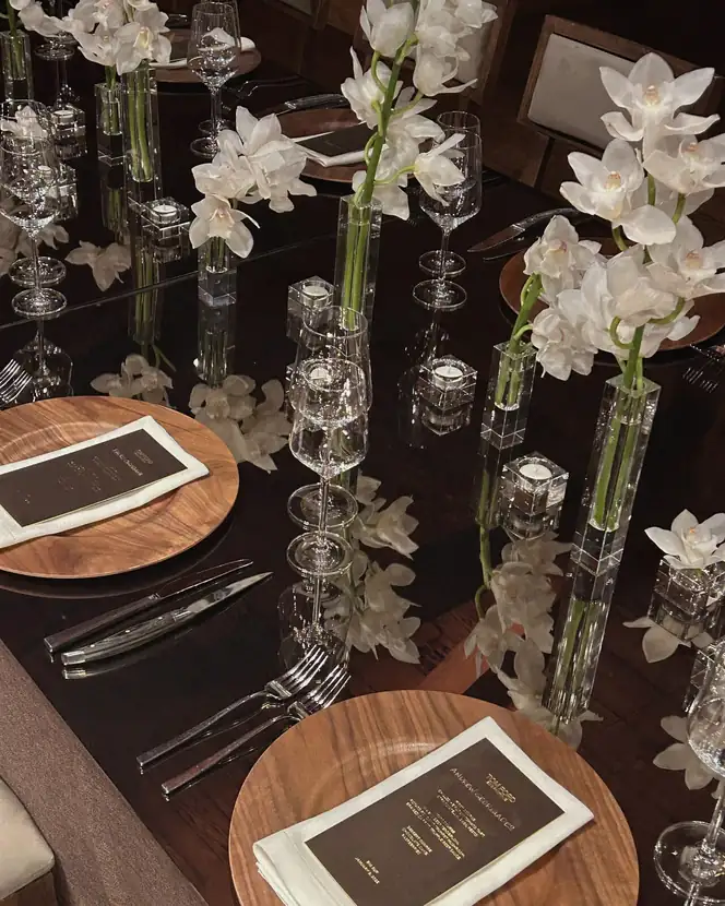 A long dinner table beneath a timber-beamed ceiling, set with orchids and low candles