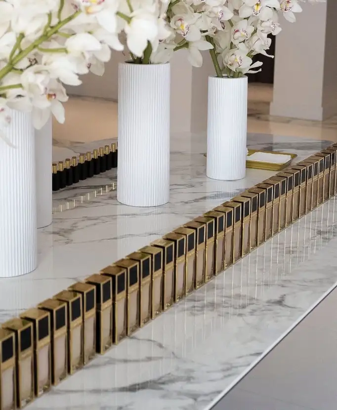 White ribbed vases and a precise row of lipsticks on a marble ledge