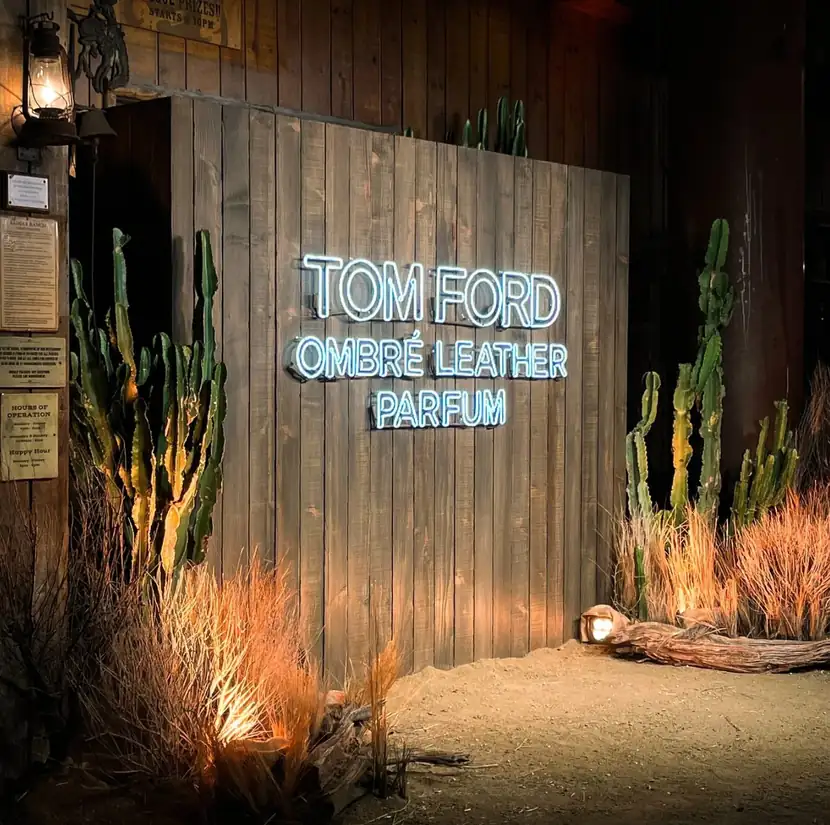 Neon Tom Ford Ombré Leather sign on a weathered timber wall amid desert cactus