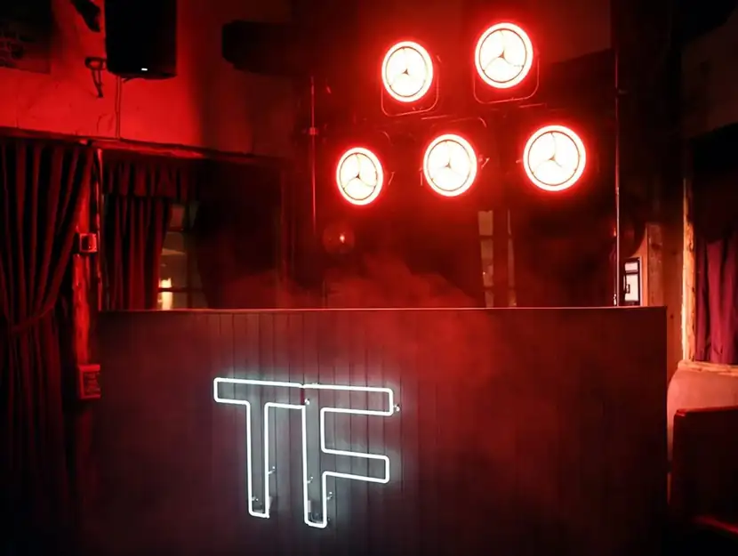 Red-lit bar with a glowing TF monogram and ring lights overhead