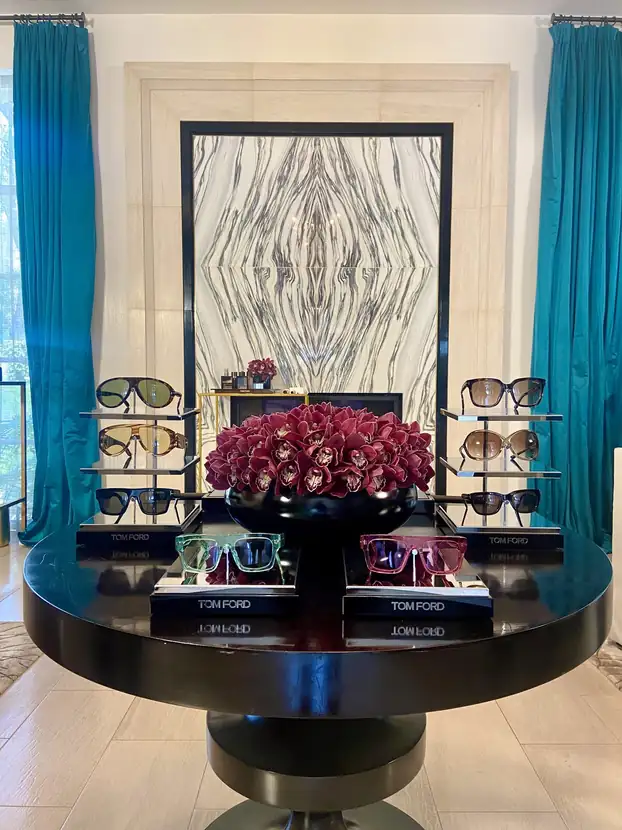 Beauty suite display of eyewear and lipstick around a deep red rose arrangement