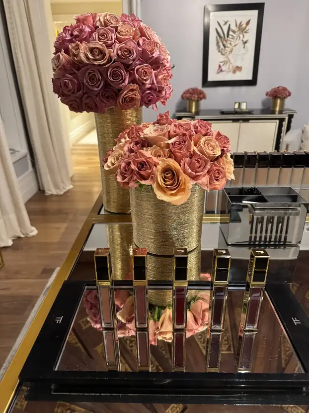 Gold vessels of blush roses staged above a mirrored lipstick display