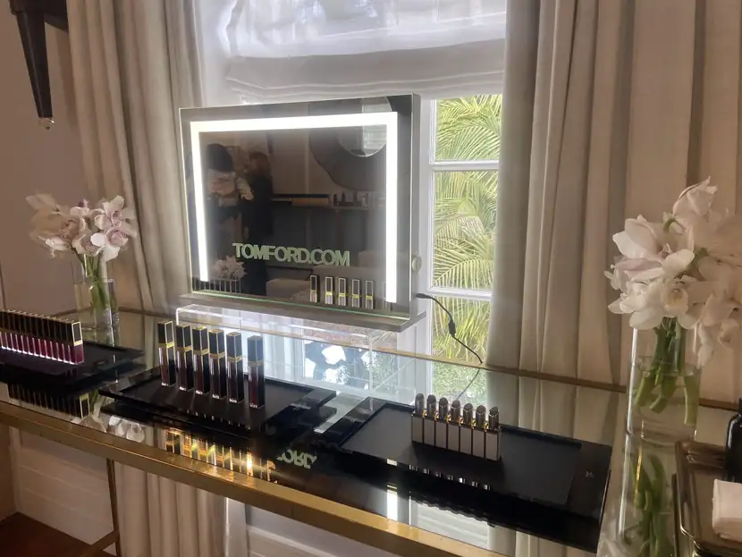 Illuminated vanity mirror above a black-and-gold lipstick display flanked by orchids