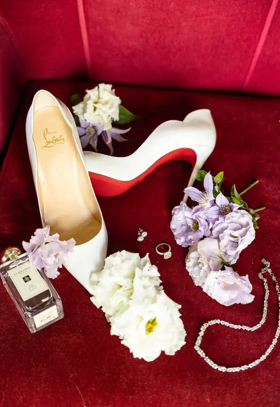 Flat lay of bridal shoes, jewelry and blush florals on crimson velvet