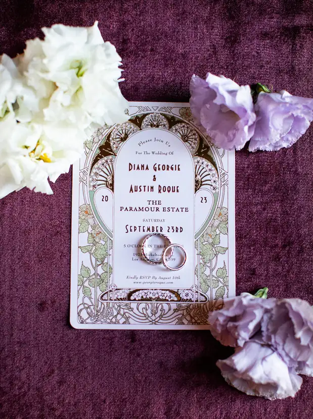 Letterpress wedding invitation and rings styled on plum velvet with white blooms