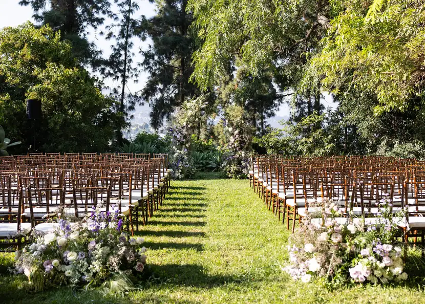 Ceremony aisle lined with chiavari chairs and low floral arrangements beneath mature trees