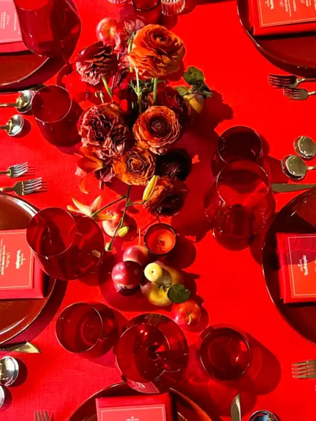 Overhead detail of red roses, apples and ruby glass on a scarlet table
